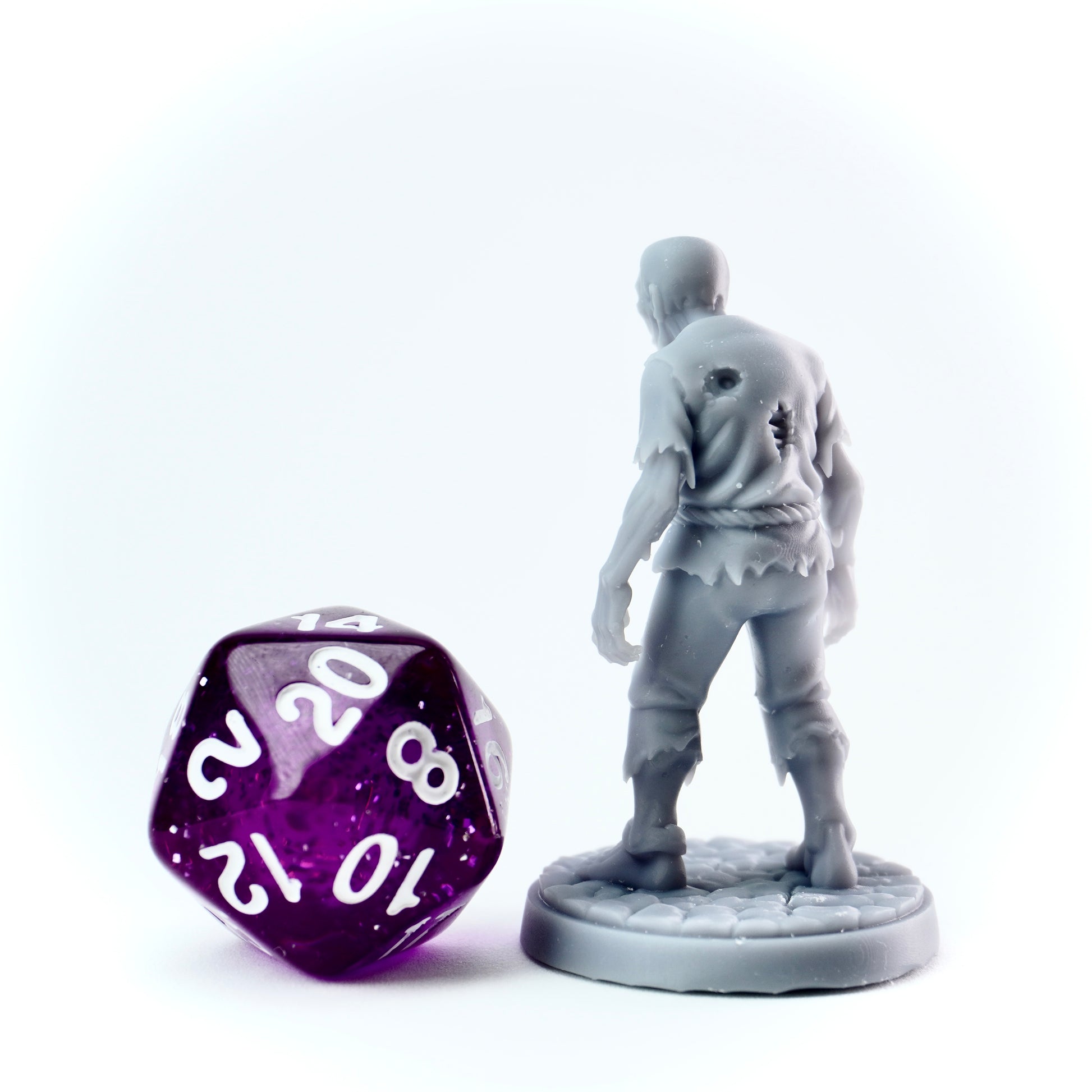 Gray zombie figurine and a purple polyhedral dice on a white background