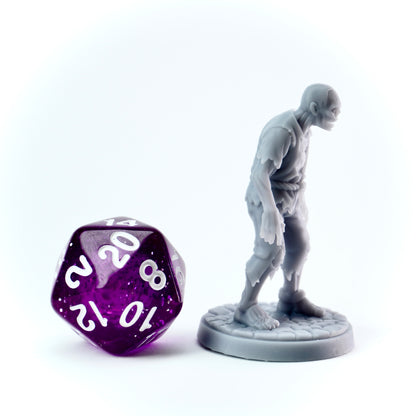 Gray zombie miniature of a humanoid standing next to a purple polyhedral dice on a white background