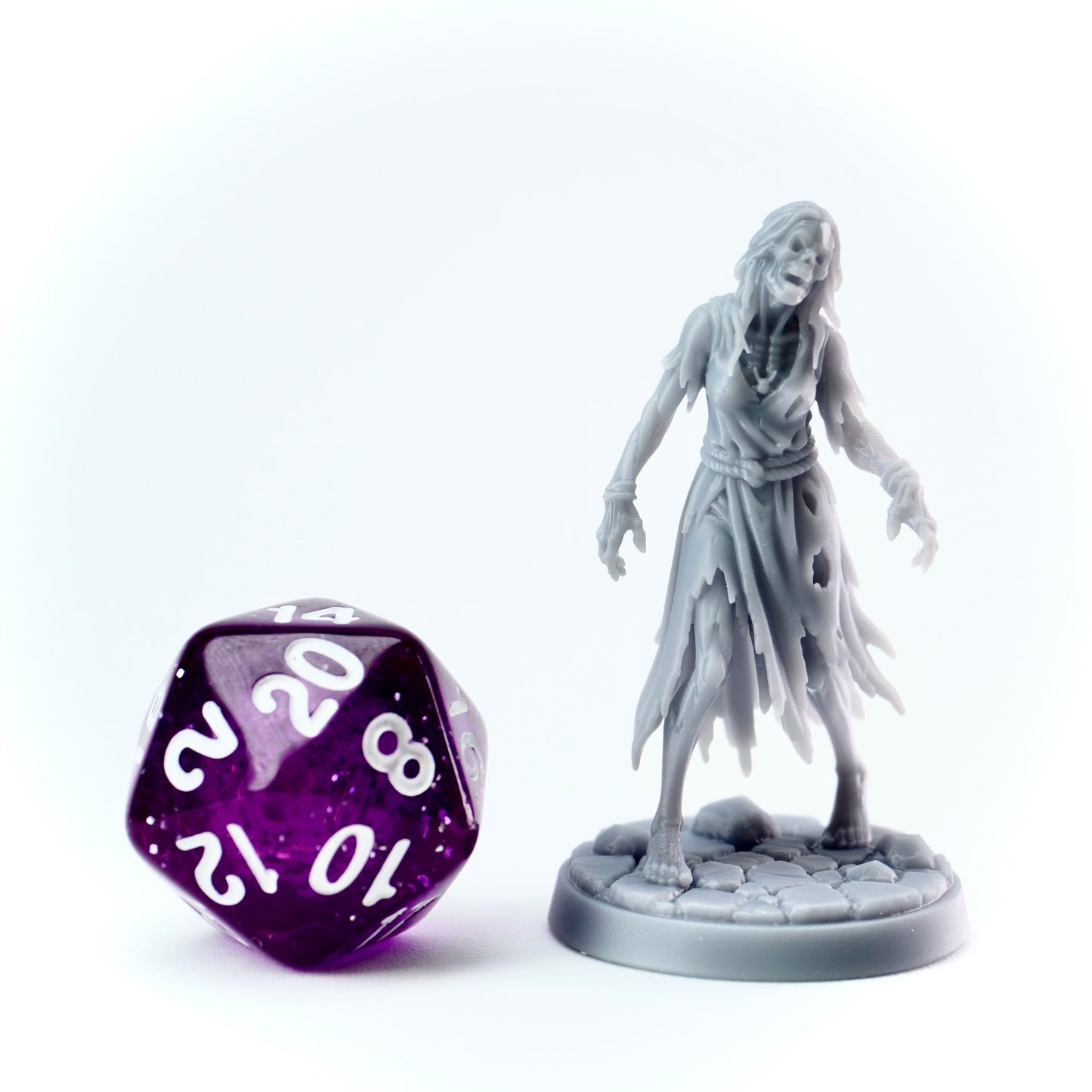 Gray zombie figurine next to a purple polyhedral dice on a white background