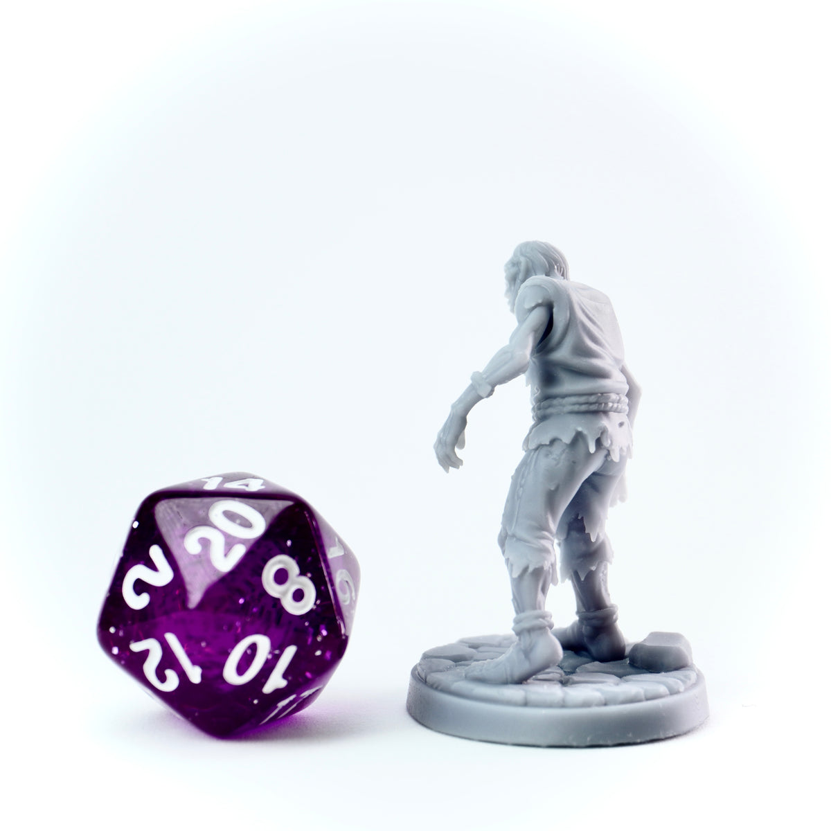 Gray miniature figure of a living dead person and a purple polyhedral dice on a white background