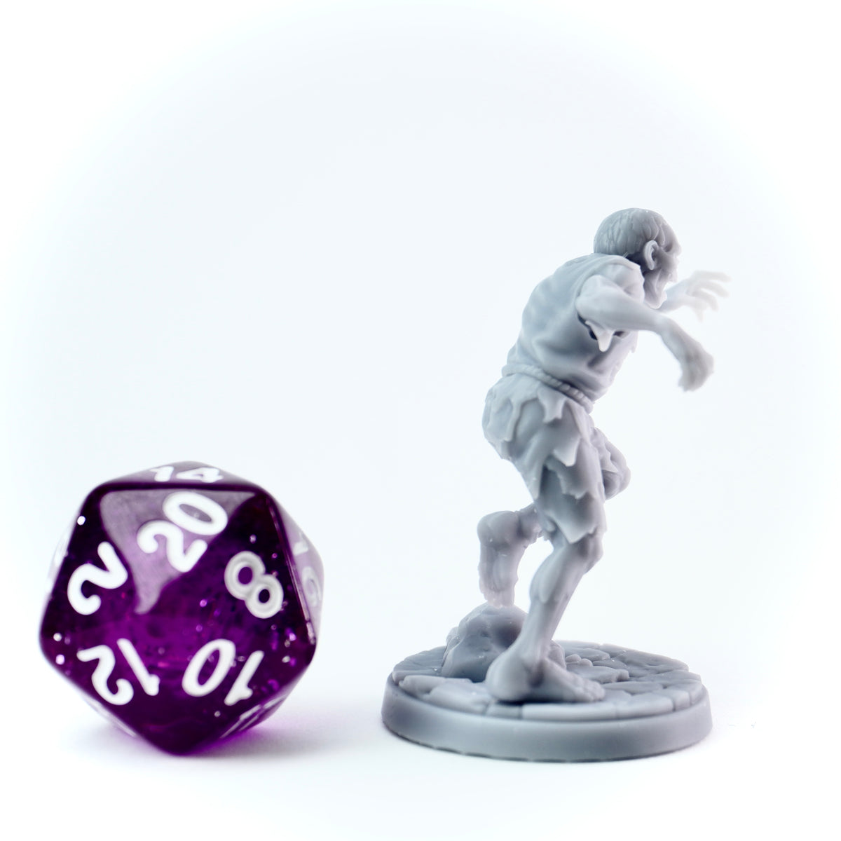 Gray miniature figure of a zombie next to a purple polyhedral dice on a white background