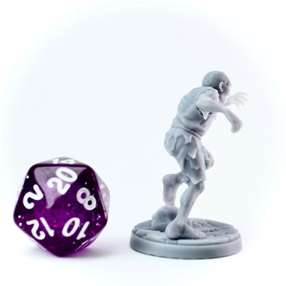 Gray miniature figure of a zombie next to a purple polyhedral dice on a white background