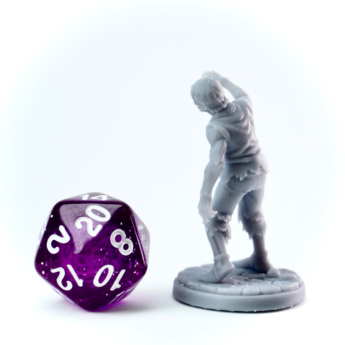 Gray figurine of a zombie character next to a purple polyhedral dice on a white background