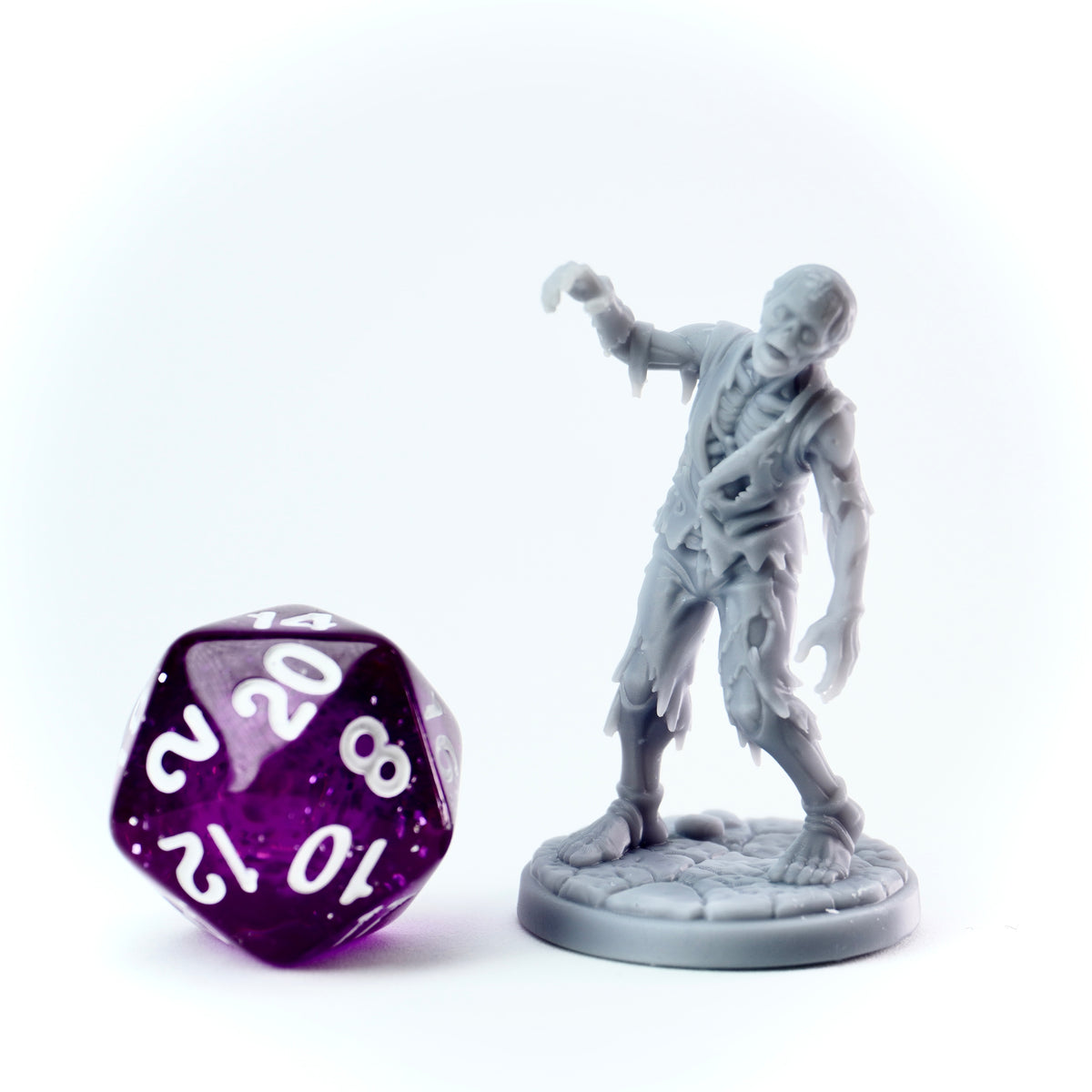 Gray zombie figurine next to a purple polyhedral dice on a white background