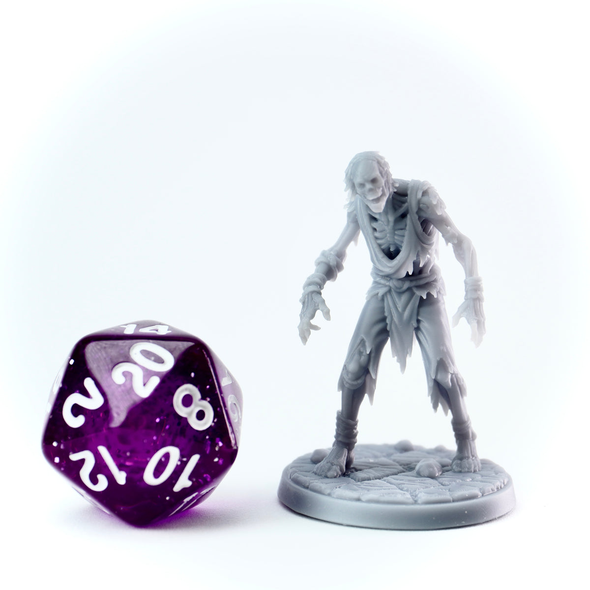 Gray zombie figurine next to a purple polyhedral dice on a white background