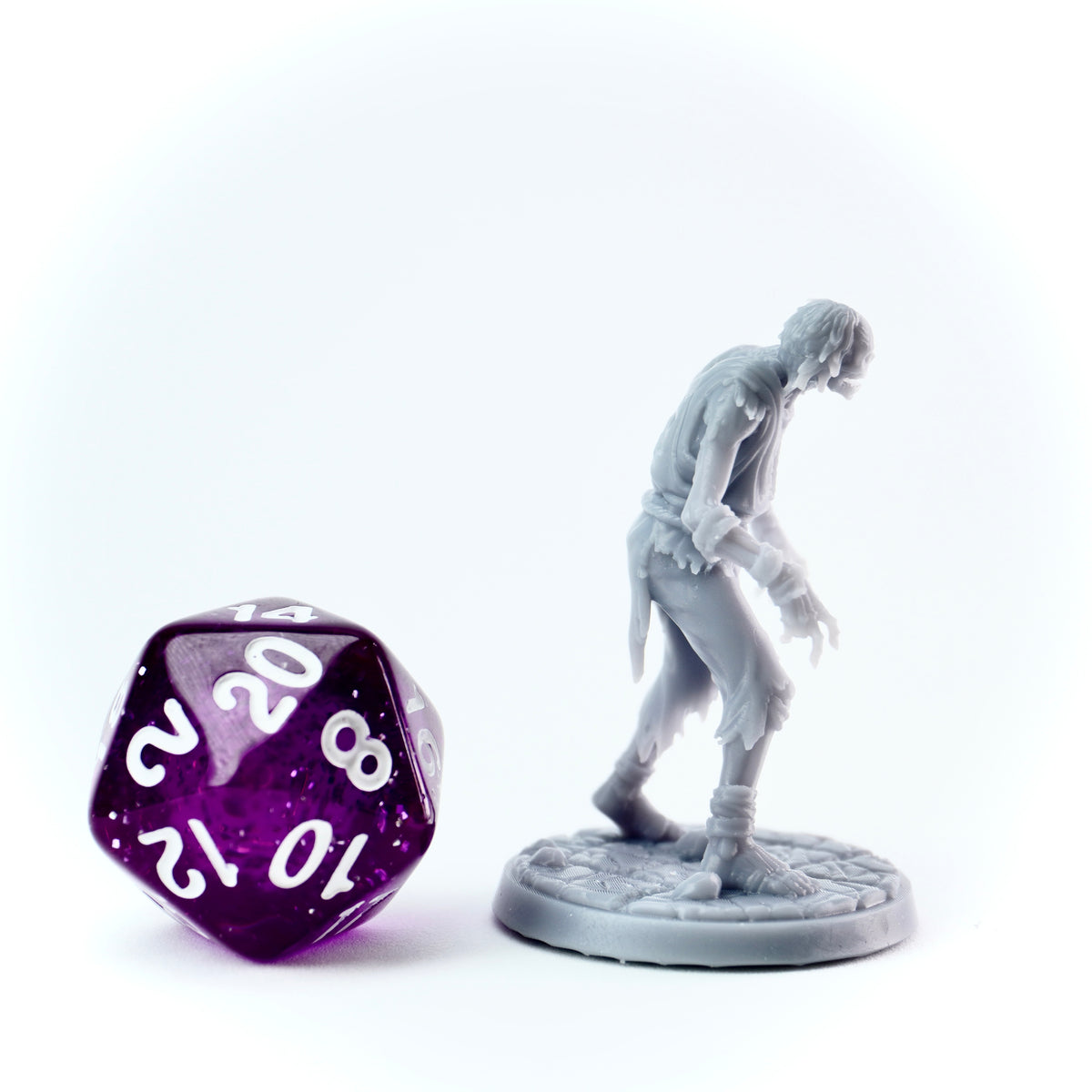 Gray miniature figure of a walking dead character next to a purple polyhedral dice on a white background