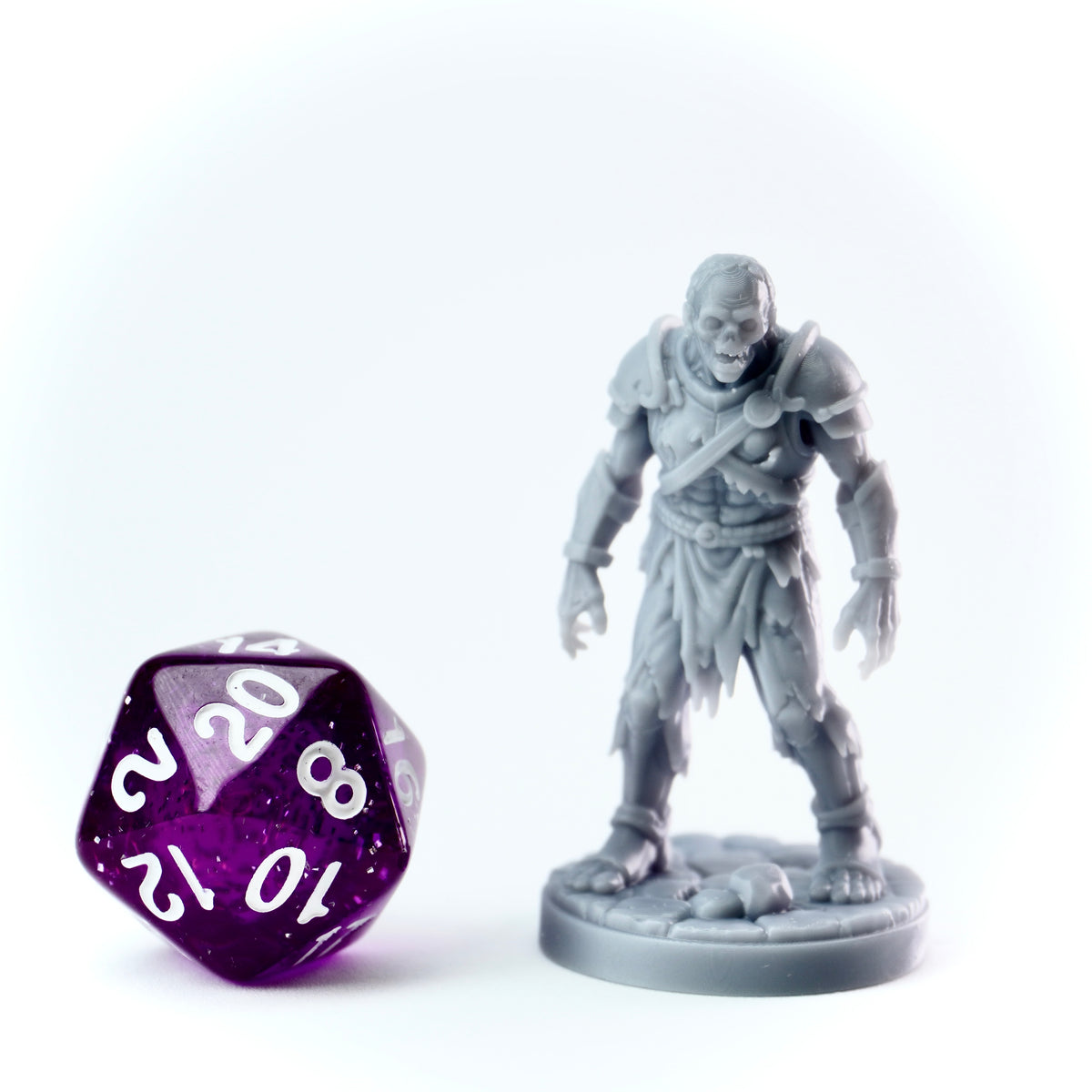 Gray zombie figurine next to a purple polyhedral dice on a white background