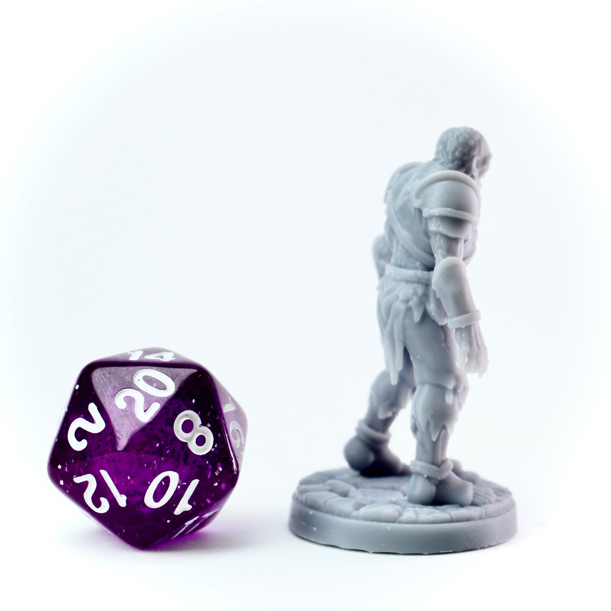 Gray miniature figure of a warrior next to a purple polyhedral dice on a white background