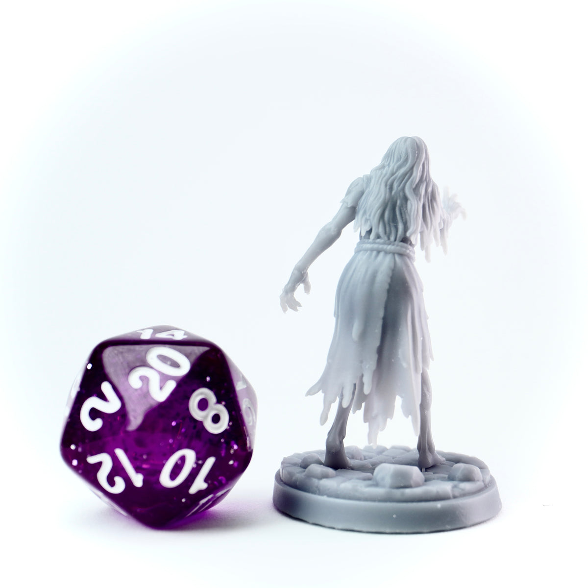 Gray figurine of a ghost-like creature next to a purple polyhedral dice on a white background